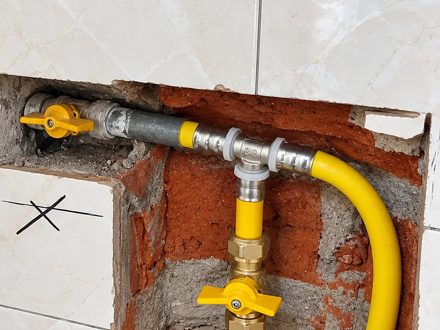 Derivación de gas con tee de bronce y válvulas de corte amarillas empotrada en el muro